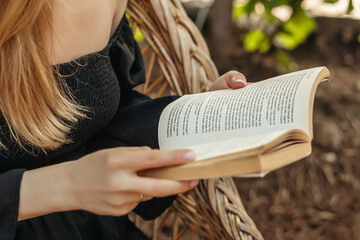 female hands holding a vintage book. girl reading a book sitting on a straw chair