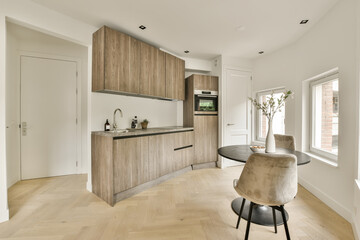 a kitchen and dining area in a house with wood flooring, white walls and wooden cabinets on the wall