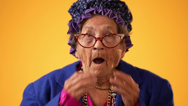 Closeup portrait of toothless funny elderly senior old woman with wrinkled skin looks at camera gives great idea gesture showing explosion of thinking posing isolated on yellow background.