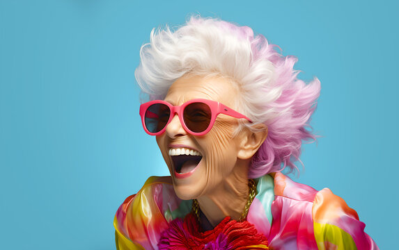 Happy senior woman in colorful outfit with funny sunglasses, laughing and smiling, trendy grandma posing in light blue studio
