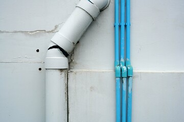 Close up a white broken plastic pipe with small blue plastic pipe on the wall of the building