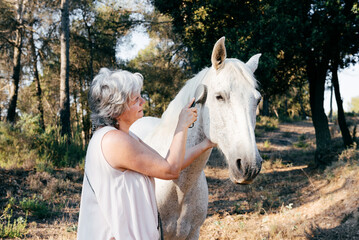 Middle aged woman brushing gray horse in countryside
