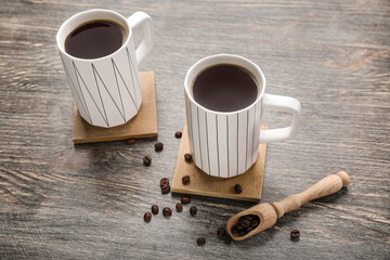 Drink coasters with cups of coffee and beans on wooden table