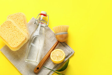 Bottle of vinegar, sponges, brush, napkin and lemon on yellow background