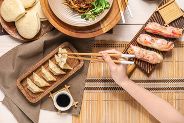 Female hand with chopsticks and tasty Chinese dishes on light wooden background