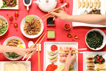 Female hands with chopsticks and different Chinese dishes on red background