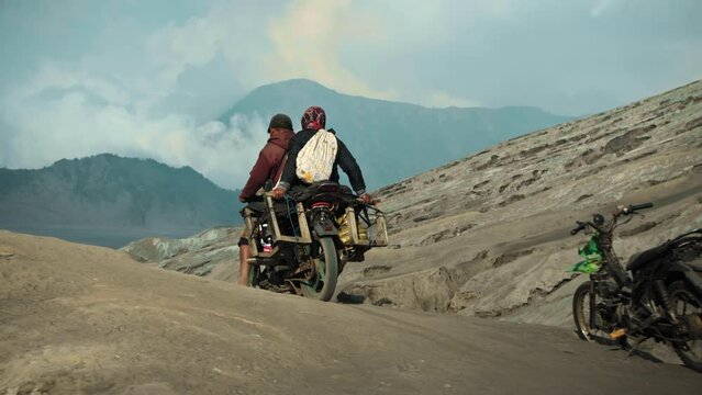 Two Indonesian people on a motorcycle ride through a volcanic desert
