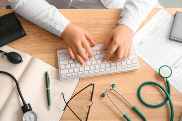Female doctor working with computer keyboard on wooden medical desk, top view - obrazy, fototapety, plakaty
