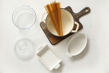 Set of kitchen utensils and pot with raw pasta on white background