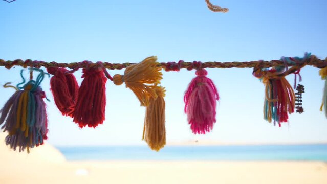Close up of decorative colorful tassels hanging on the rope in bedouin tent in the desert. Sandy beach in the blurred background