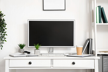 Modern workplace with blank computer monitor and artificial plants in light office