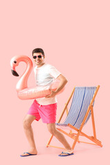 Young man with swim ring and deck chair on pink background