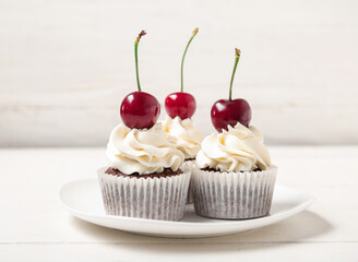 Plate with tasty cherry cupcakes on table