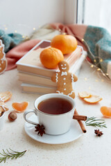 Cozy seasonal food - aesthetics coffee, gingerbread cookies, tangerines near books on the window. Christmas holidays mood in snowy day