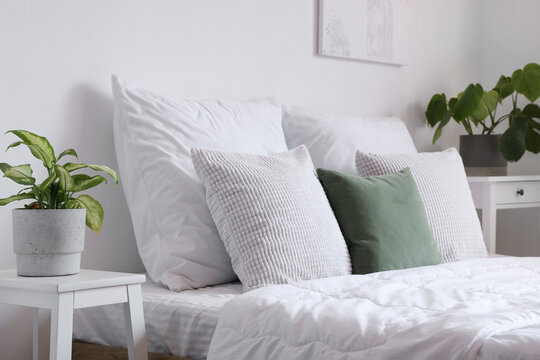 Cozy bed with white blanket and pillows in light bedroom