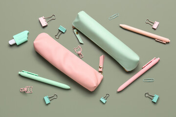 Pencil cases with school stationery on green background
