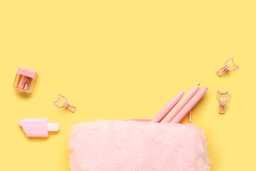 Pink pencil case with school stationery on yellow background