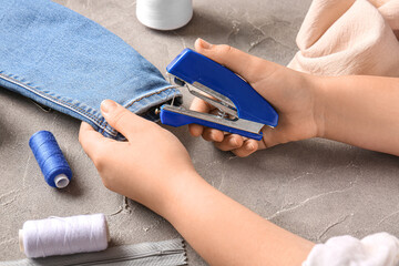 Female hands with different supplies sewing jeans on grunge grey background © Pixel-Shot