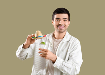 Young man with tequila shot and sombrero hat on green background