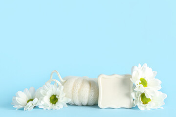 Soap bar, bath sponge and chamomile flowers on color background