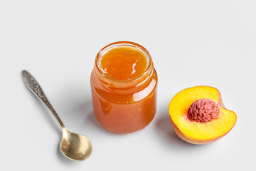 Glass jar of tasty peach jam and spoon on light background