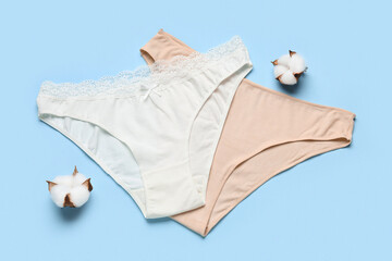 Female panties and cotton flowers on color background