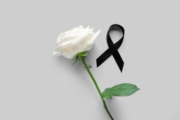 Beautiful rose flower and black funeral ribbon on grey background
