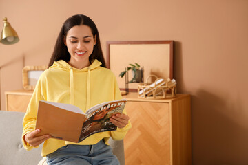 Young woman in hoodie reading magazine at home