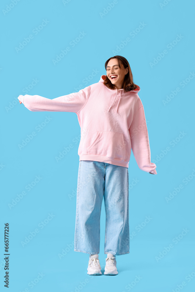 Wall mural young woman in pink hoodie on blue background