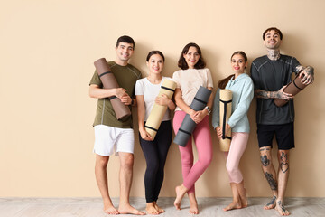 Fototapeta na wymiar Group of sporty young people with yoga mats near beige wall