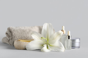 Fototapeta na wymiar Set of cosmetic products, clean towel and beautiful lily flower on grey background