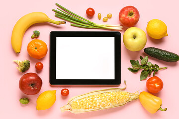 Tablet computer with fruits and vegetables on pink background