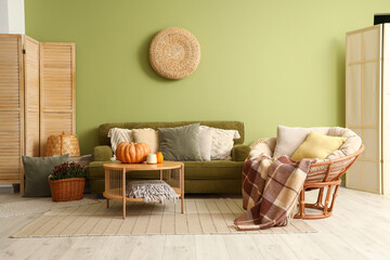 Interior of stylish living room with green sofa, pumpkins on coffee table and armchair