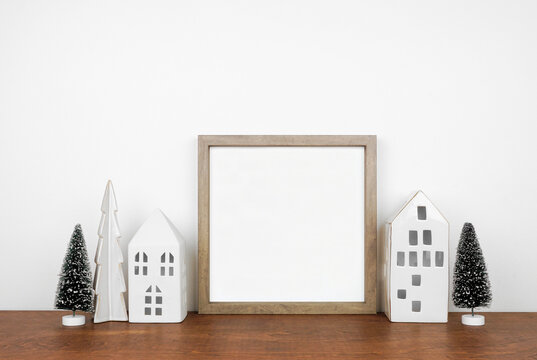 Christmas mock up with wooden frame, trees and white house decor. Square frame on a wood shelf against a white wall. Copy space.