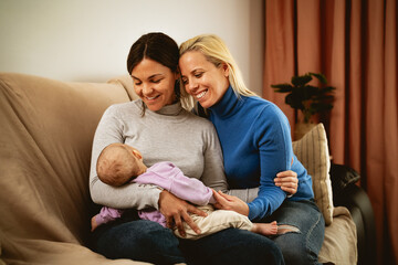 Happy lesbian couple taking care of her small baby at home - LGBT Family and maternity concept - obrazy, fototapety, plakaty