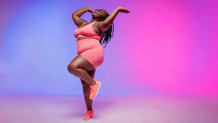 Full length of joyful voluptuous African woman in sportswear dancing and smiling 