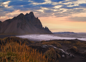 Sunrise Stokksnes cape sea beach and Vestrahorn Mountain, Iceland. Amazing nature scenery, popular travel destination. Autumn grass on black volcanic sand dunes.