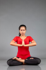 Healthy young woman in red t-shirt and black leggings doing yoga and stretching exercises isolated on grey background