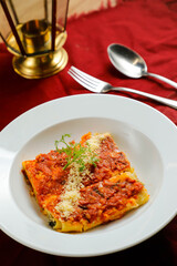 Spicy Tomato and Beef Lasagna served in plate with fork and spoon isolated on red napkin side view of fast food on table