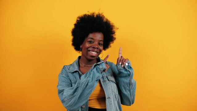 Young African American woman points upper right corner isolated over vivid yellow background. Girl shows direction or way. Lifestyle concept