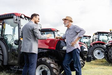 Farmer and dealer shaking hands after successful tractor purchase. Investing in farming equipment.