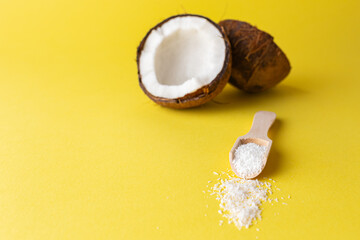 Coconut halves with wooden spoon and coconut flour isolated on yellow background. Space for copy