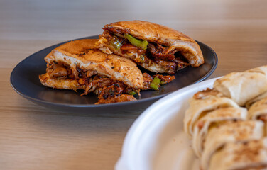 Italian pieces of shawarma full of peppers and BBQ sauces with chicken on nad shawarma pieces on wooden table with black plates