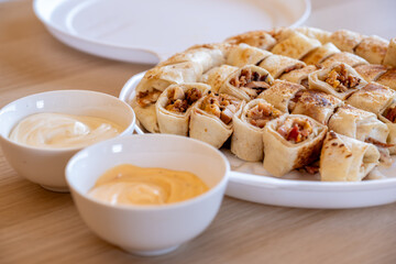 Pieces of shawarma on wooden table with dips and arranged on white plate