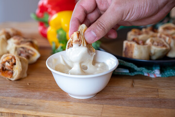 hand holding shawarma piece and dip it in mayonnaise or garlic tahini with shawarma plate and peppers behind