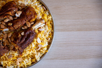 Plate of meat and rice topped with almonds on wooden table with top view