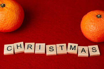 the word Christmas composed of wooden letters on a red background with tangerines
