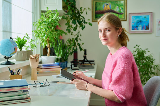 Portrait of teenage girl student looking at camera sitting with digital tablet at home