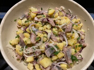 Salad of smoked herring, potatoes and onions presented in a round dish in front of a black background