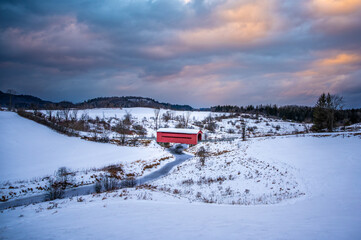 Red covered bridge in the Meech Creek Valley during winter, with colourful dramatic cloudy sunset...